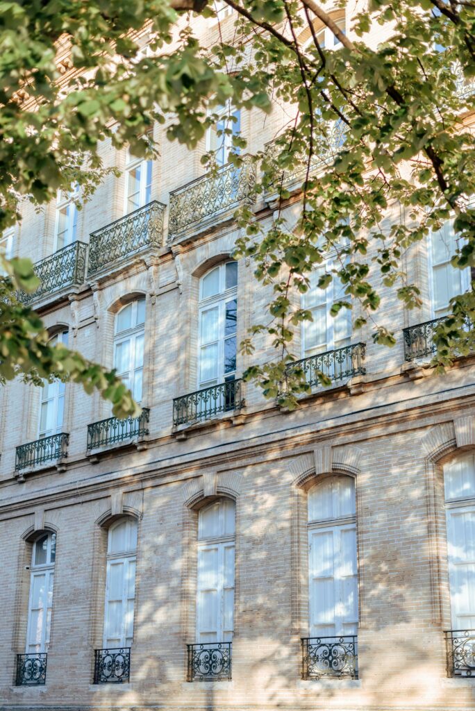 Sunlit view of a classic French building with ornate ironwork and brick facade in Toulouse.