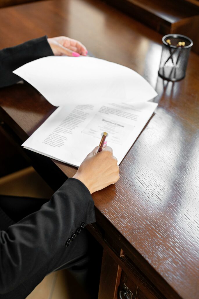 Close-up of a business professional signing a paper document at a wooden desk.